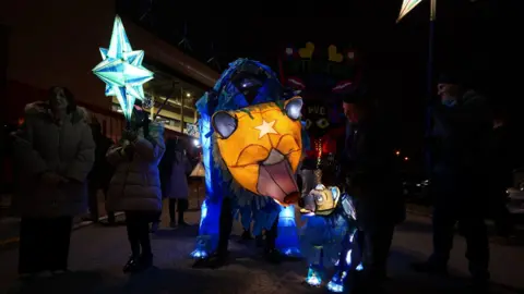 PA Media A lit-up lantern bear next to a smaller one, with people holding lit up stars in the dark