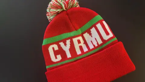 BBC A red bobble hat with a misspelt Welsh word across the front