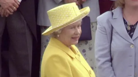 Getty Images/Tim Graham The late Elizabeth II attending a garden party at Buckingham Palace in July 2000.  She is wearing a bright yellow coat dress, a matching hat and pearl earrings.  