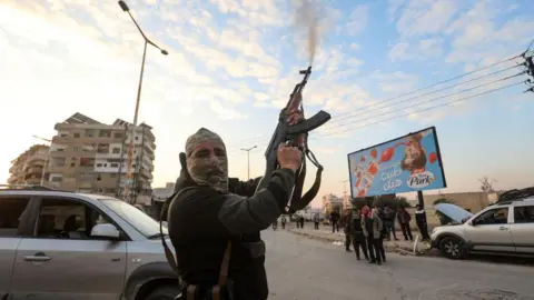 AFP A Syrian rebel fighter fires into the air in the city of Hama, Syria (5 December 2024)