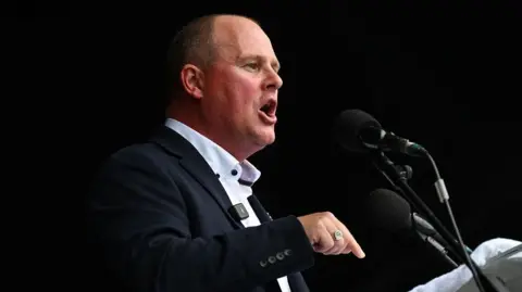 Getty Images TUC general secretary Paul Nowak addresses the Durham Miners' Gala, dressed in a dark suit with an open neck shirt. He is making a point with his finger and speaking into two microphones