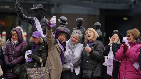 PA Media Seven women stand in front of a statue 