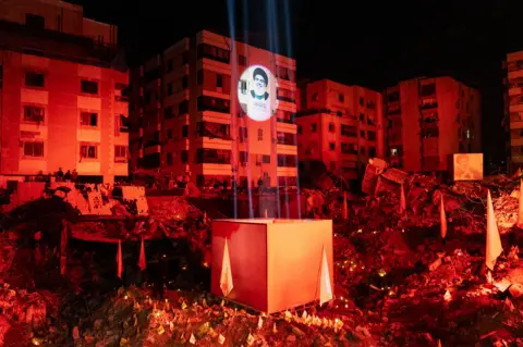 Joel Gunter/BBC The crater left behind by the Israeli air strike that killed Hassan Nasrallah was lit up in red for the event.