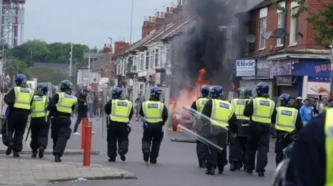 PA Media Riot police in Middlesbrough during the summer riots. A property is on fire.