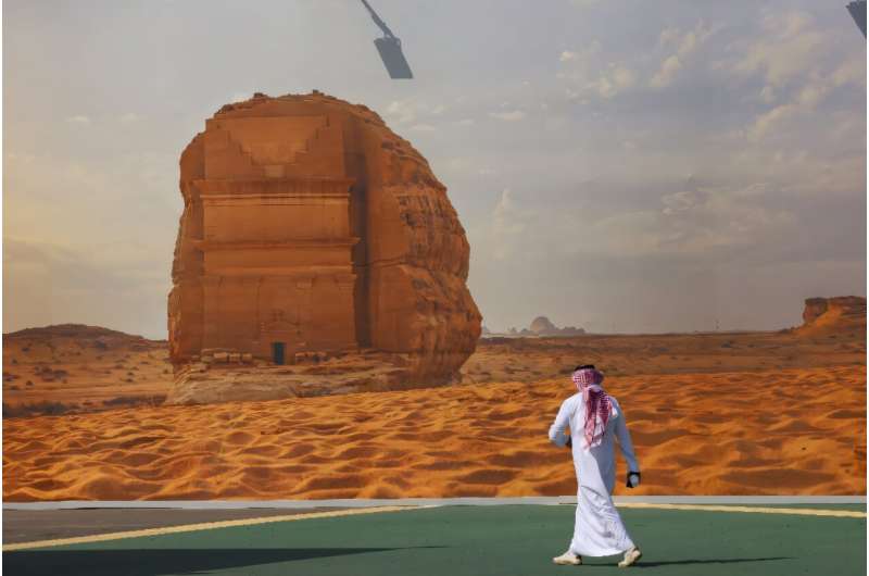 A COP16 delegate walks past a giant poster of a Saudi archaeological site at the start of the UNCCD talks