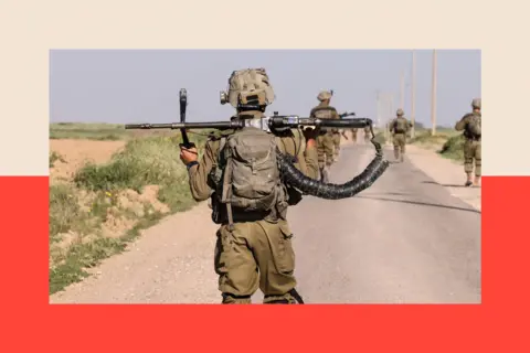 Getty Images Israeli soldiers walk near the border with Gaza Strip in southern Israel, they wear green camouflage and weapons are shown