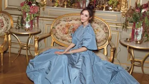 Family handout Ms Huang poses on an ornate sofa in a palatial room wearing an enormous blue ballgown