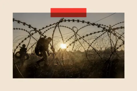 Reuters Soldiers walking alongside barbed wire as the sun sets