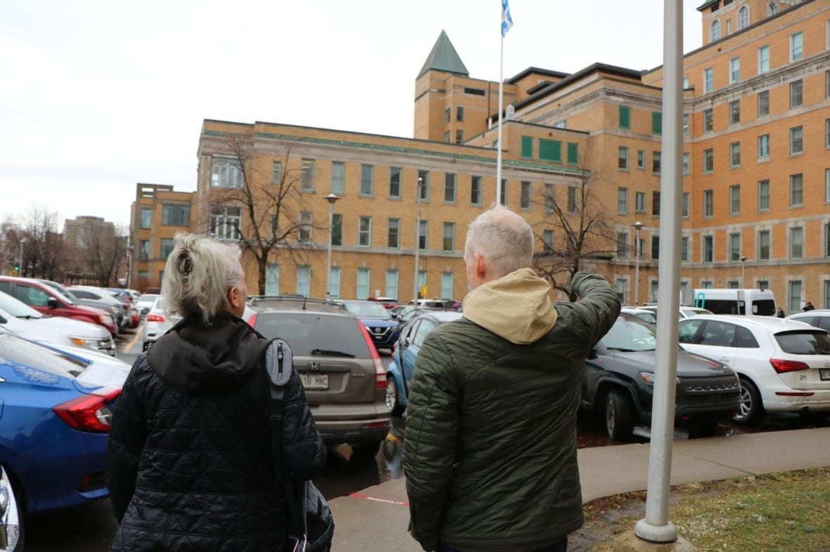 A picture taken from behind two people outside of a hospital. 