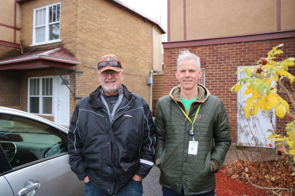 Two men standing next to each other outside of a building. 