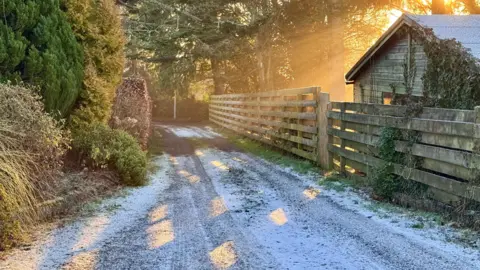 BBC Weather Watchers/Nellington The sun shines from behind some trees on a frosty road