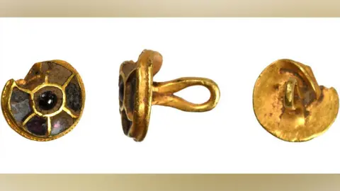 West Yorkshire Archaeology Advisory Service Three views of an Anglo-Saxon gold and red stone button or stud, slightly damaged on its top edge. The first view on the left shows the front, which is round and has six compartments on its face, which were inlaid with red stones - some still existing. The middle view shows its side and the gold loop attached to its back. The third view on the right is of its back, which is entirely gold and has the loop facing to the viewer. 