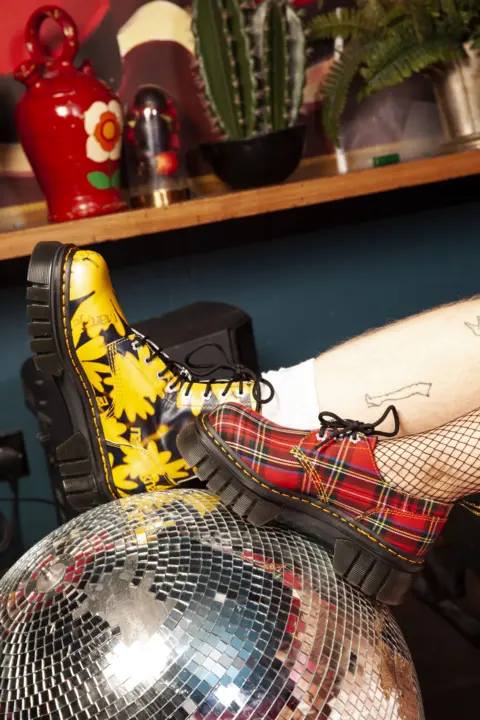 Megan Winstone A red chequered Dr Marten boot and a yellow and clack floral Dr Marten boot on a glitter ball