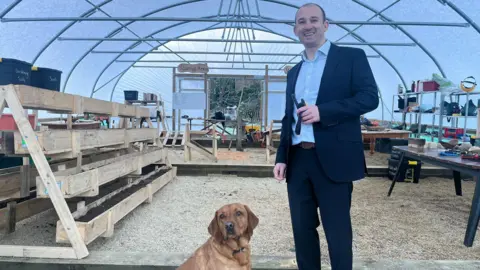 Hope Rhodes / BBC Headteacher Dan Crossman and the school's therapy dog Woody, standing in the school's forest school