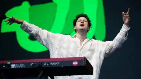 Getty Images Barry Can't Swim on stage behind a keyboard with his arms in the air in front of a large green graphic