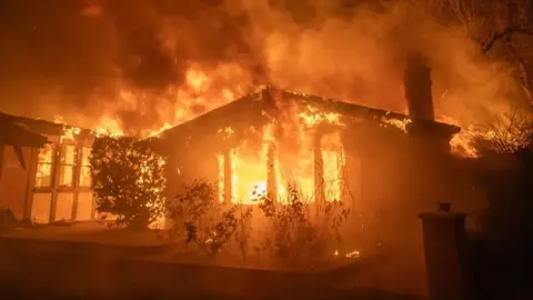 Getty Images A house on fire in the Palisades neighbourhood after strong winds and dry conditions saw multipl; conflagrations ignite. 