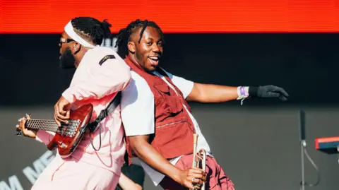 Sarah-Louise Bennett / BBC TJ Foleoso (left) and Ife Ogunjobi (right) of Ezra Collective share an on-stage moment at the 2024 Glastonbury Festival