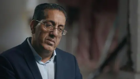 Nazir Afzal being interviewed by the BBC. He is wearing an open-necked shirt and jacket. 