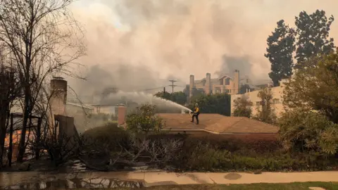 Lucy Sherriff A fireman houses down a fire while standing on a roof