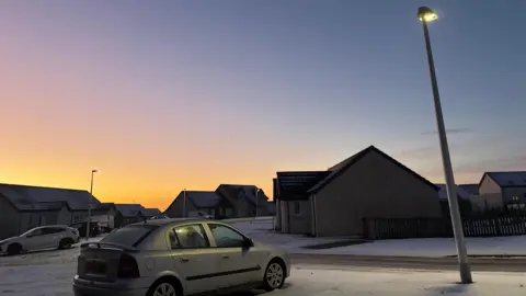 BBC Weather Watchers - Ed Car parked on snow beside a lamp post