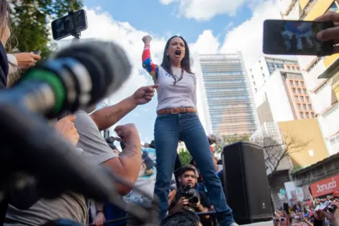 Jonathan Lanza/NurPhoto via Getty Images Venezuelan opposition leader Maria Corina Machado addressing a protest rally, with her arm raised in the air as she speaks