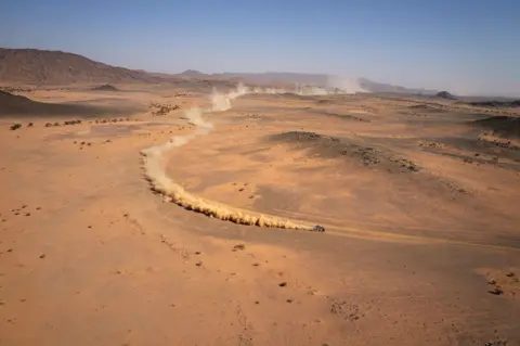 Valery HACHE / AFP A car is followed by a dust trail in the Saudi desert, as it takes part in the Dakar Rally.