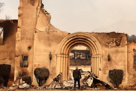 Christina House / Los Angeles Times via Getty Images A man stands and looks at the remains of the Altadena Community Church, burned down by the Eaton fire