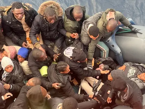 SALVAMENTO MARITIMO/Handout via REUTERS A migrant holds a newborn baby as a woman lies inside a rubber boat with other migrants who were rescued off the Canary Islands