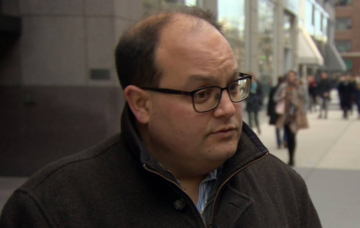 Balding man wearing glasses outdoors with a jacket on.