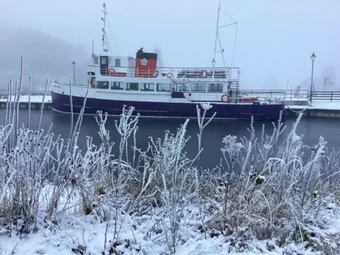 BBC Weather Watchers/Lochnessmonster A boat moored in a lake with fog behind a bank covered of tall grasses in snow and frost