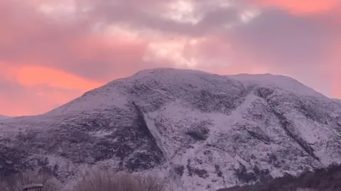 BBC Weather Watchers/JaneK A snow covered mountain against an orange and pink sky