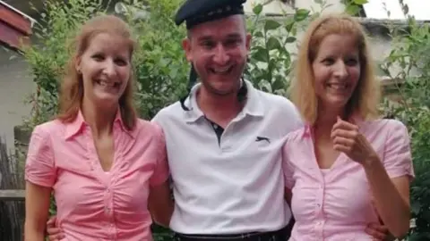 Huszti Family Two twin sisters wearing pink tops, either side of a man in a white top.