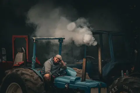 Bobby Ford A farmer sits on his tractor with smoke coming from the exhaust