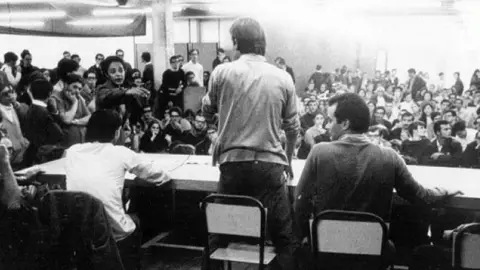 Marta Costta/Family handout Large number of university students in a room; Helenira stood up and pointing at someone