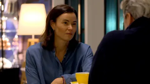 Maliina Abelsen sitting at a table wearing a blue shirt with a yellow cup in front of her