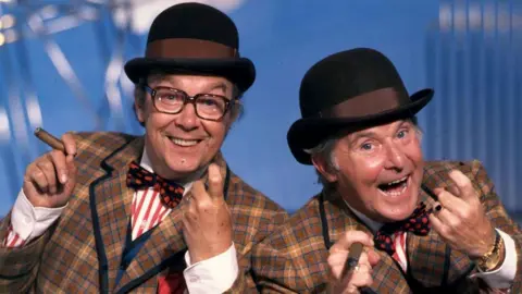 Getty Images Comedians Eric Morecambe and Ernie Wise dressed in checked suits, bowler hats and holding cigars during a rehearsal for their series The Morecambe & Wise Show, circa 1981