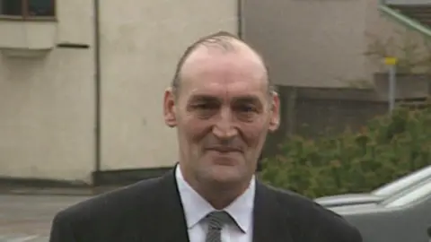 Michael Bowen, wearing a dark suit, looks into the camera as he arrives at Newport crown court for his trial.