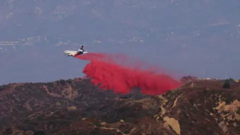 Getty Images An image showing an airtanker dropping bright red fire retardant onto hills in California 