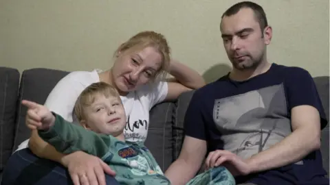 Svitlana, Dima and their four-year-old son Vova sit on their sofa. 