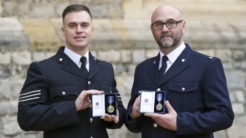 PA Media Sgt Michael Hooper, (left) and Constable Stephen Quartermain in their full uniform with navy jackets, white shirts and black ties, holding their medals.