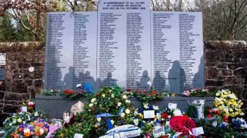 PA Media Wreaths and floral tributes in front of the Lockerbie bombing memorial, a large grey granite structure containing the names of the victims