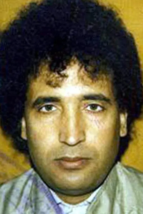 Crown Office Abdulbasset Al Megrahi looking straight at the camera. He has black curly hair and there is a yellow background.