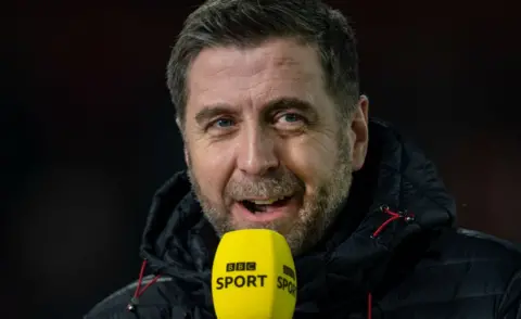 Getty Images Mark Chapman holding a BBC Sport microphone in an outdoors coat before the Premier League match between Sheffield United and Manchester United at Bramall Lane on November 24, 2019