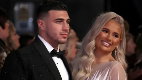 Getty Images Tommy Fury in a black suit and Molly-Mae Hague in a light coloured dress