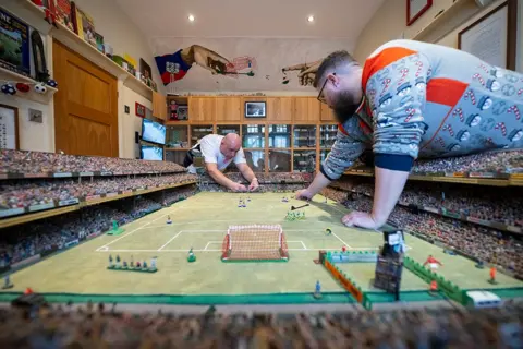 Justin Setterfield/Getty Images Subbuteo enthusiasts play on handmade tables in the house of Stephen Morton on December 29, 2024 in Essex, England. 