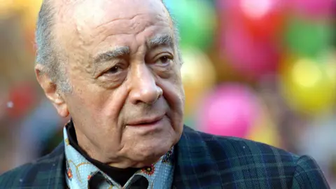 Getty Images Close up head and shoulders portrait of Mohamed Al Fayed looking to the left of camera wearing a suit and shirt, with festive colouful balls out of focus in the background. Image taken at Harrods in London in 2007.