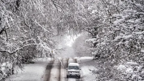 PA Media A 4x4 makes its way through a snow-covered road in Scotton, Harrogate, North Yorkshire