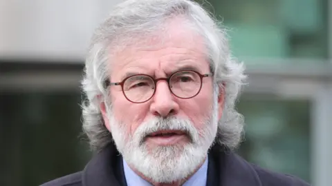 Niall Carson/PA Gerry Adams is looking to the right of the camera. He has circular dark red glasses and a grey beard and hair down to his shoulder. 