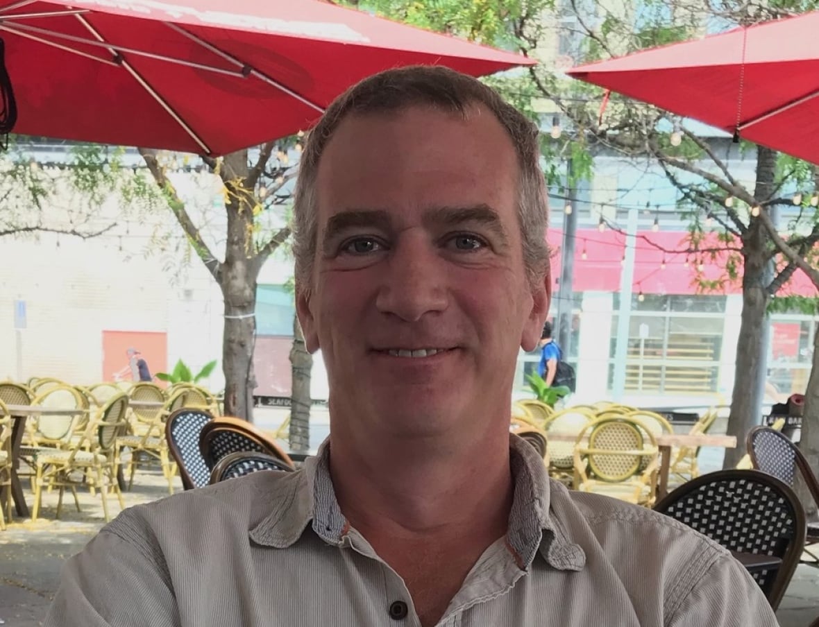 A smiling man wearing a white shirt.