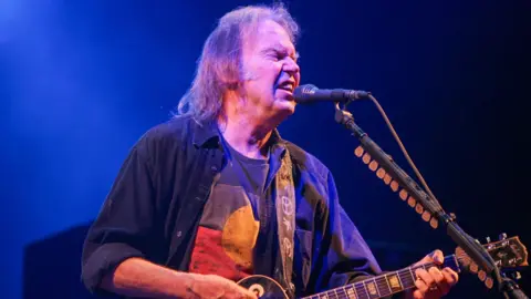 Getty Images Neil Young playing his guitar and singing on-stage at Glastonbury Festival in 2009